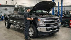 Mechanic diagnosing a diesel pickup with a scan tool in a repair workshop.