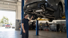Mechanic inspecting the curved exhaust system beneath a car on a professional lift